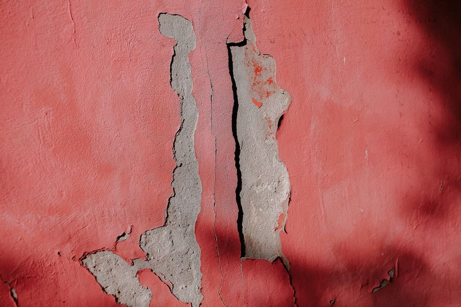 美人祭 — Cracked red wall surface showcasing peeling paint and exposed cement texture.