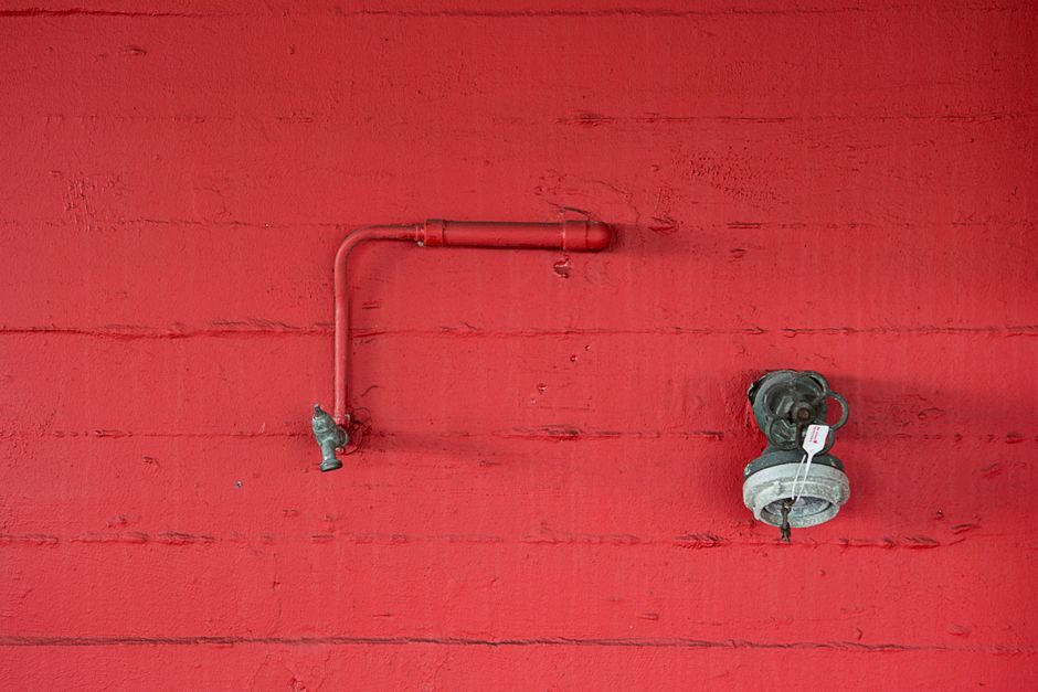 朱草 — Close-up of a red wall featuring an industrial faucet and pipeline. Minimalist design.